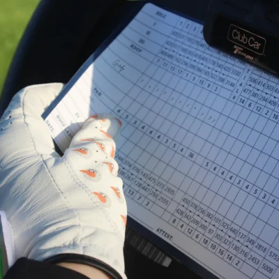 Gloved hand in the Gurdy-print Birdie Chaser Style 2 glove filling out a Club Car golf cart scorecard